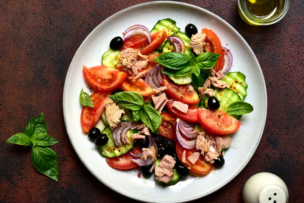 Brightly coloured Mediterranean salad with tomatoes, cucumber, leaves, olives, tuna and herbs